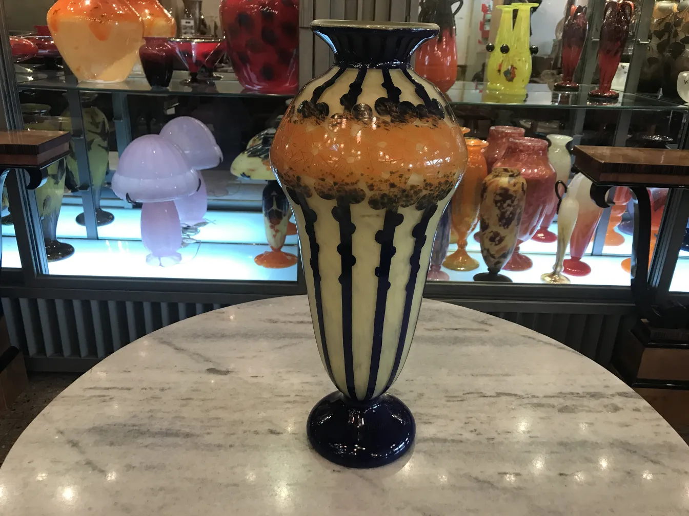 Vase ancien en verre signé Le Verre avec des décorations colorées uniques, exposé parmi d'autres antiquités.