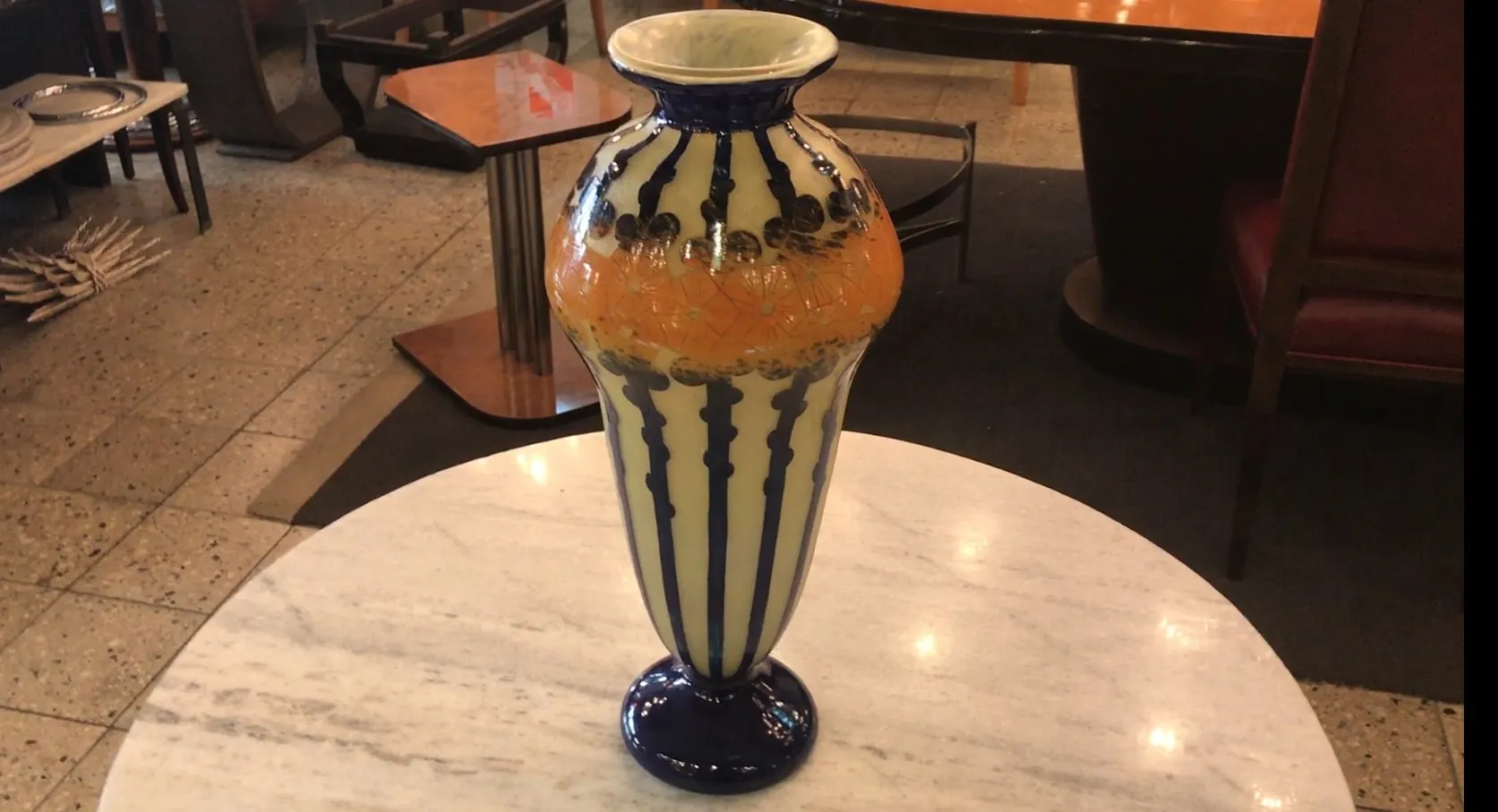 Vaso antico in vetro firmato Le Verre, decorato con colori vivaci su sfondo chiaro, su un tavolo.