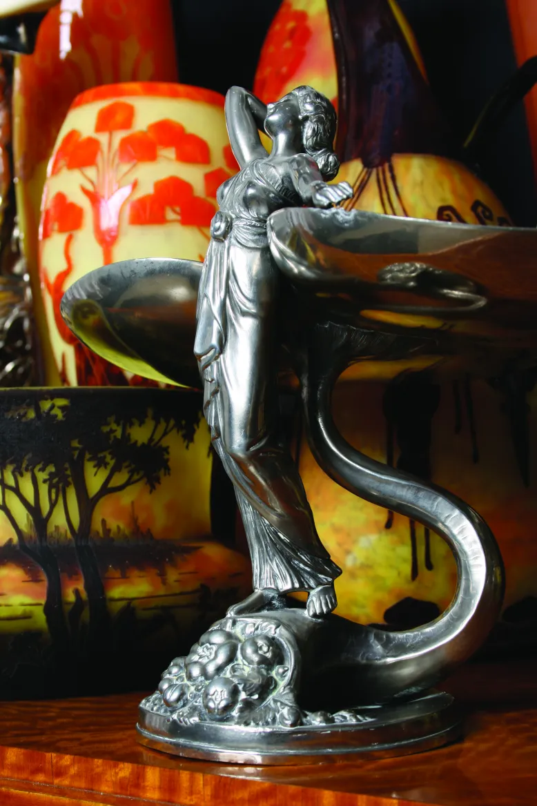 Metallskulptur einer weiblichen Figur, Glaskunst im Hintergrund