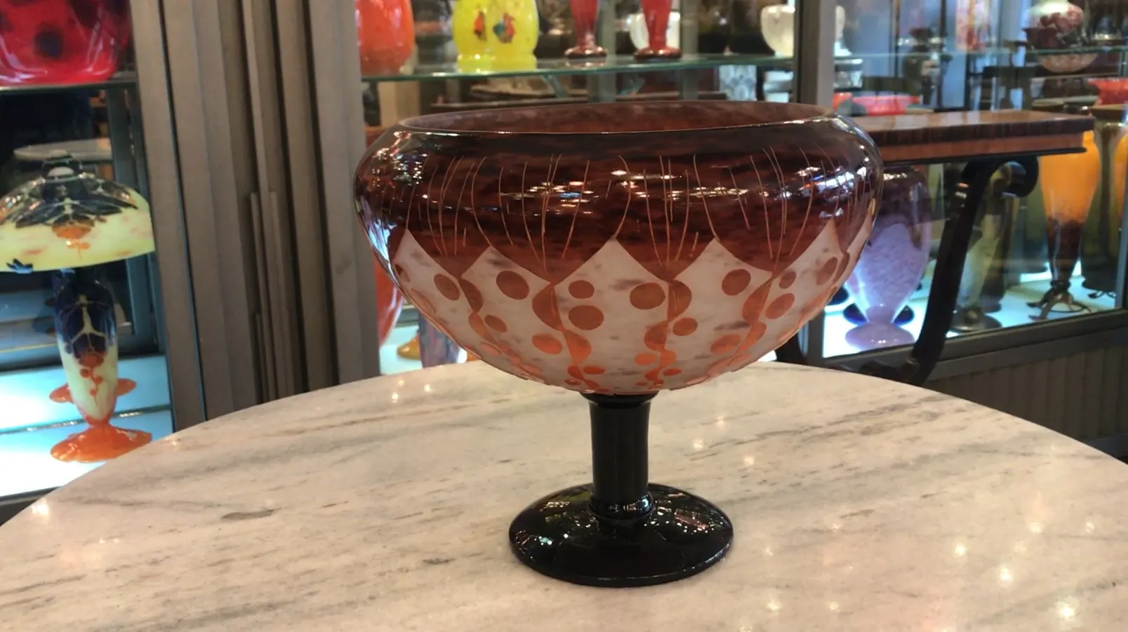 Vetro firmato Le Verre con design decorativo in tonalità calde, in un ambiente di antiquariato.
