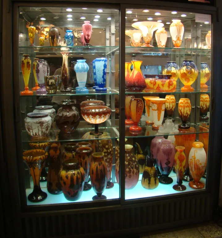 Vitrine com várias antiguidades de vidro assinado Le Verre em diferentes cores e formas.