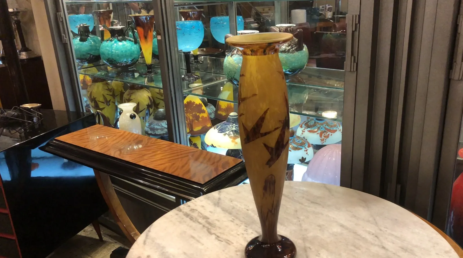 Antique signed glass Le Verre with artistic shapes and designs. Background features colorful antiques.