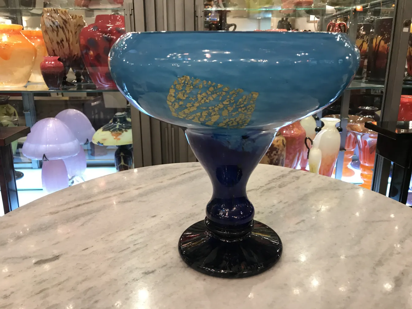 Vaso blu con firma visibile, base nera e decorazioni dorate, circondato da altri oggetti antichi.