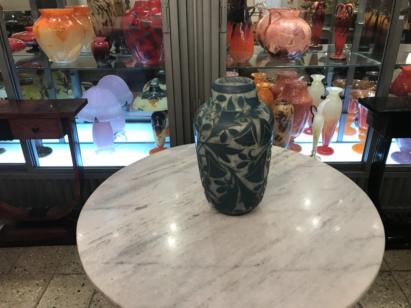 Vidrio antiguo firmado Daum Nancy en una mesa de mármol con otros objetos decorativos de fondo.