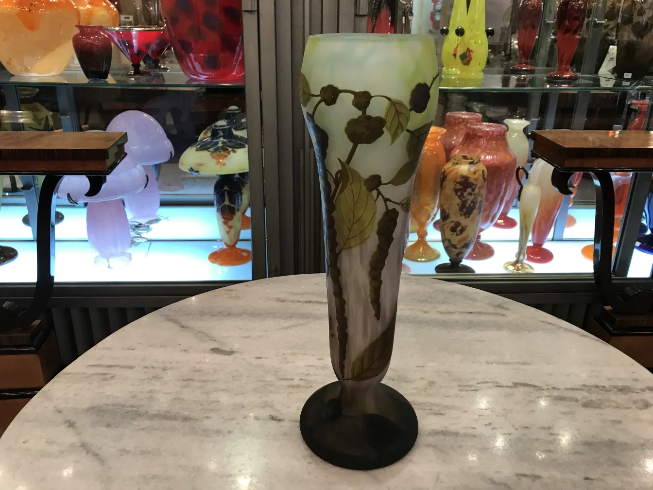 Un vaso alto con diseño de hojas y frutos, fondo difuminado, exhibido en un ambiente vintage.