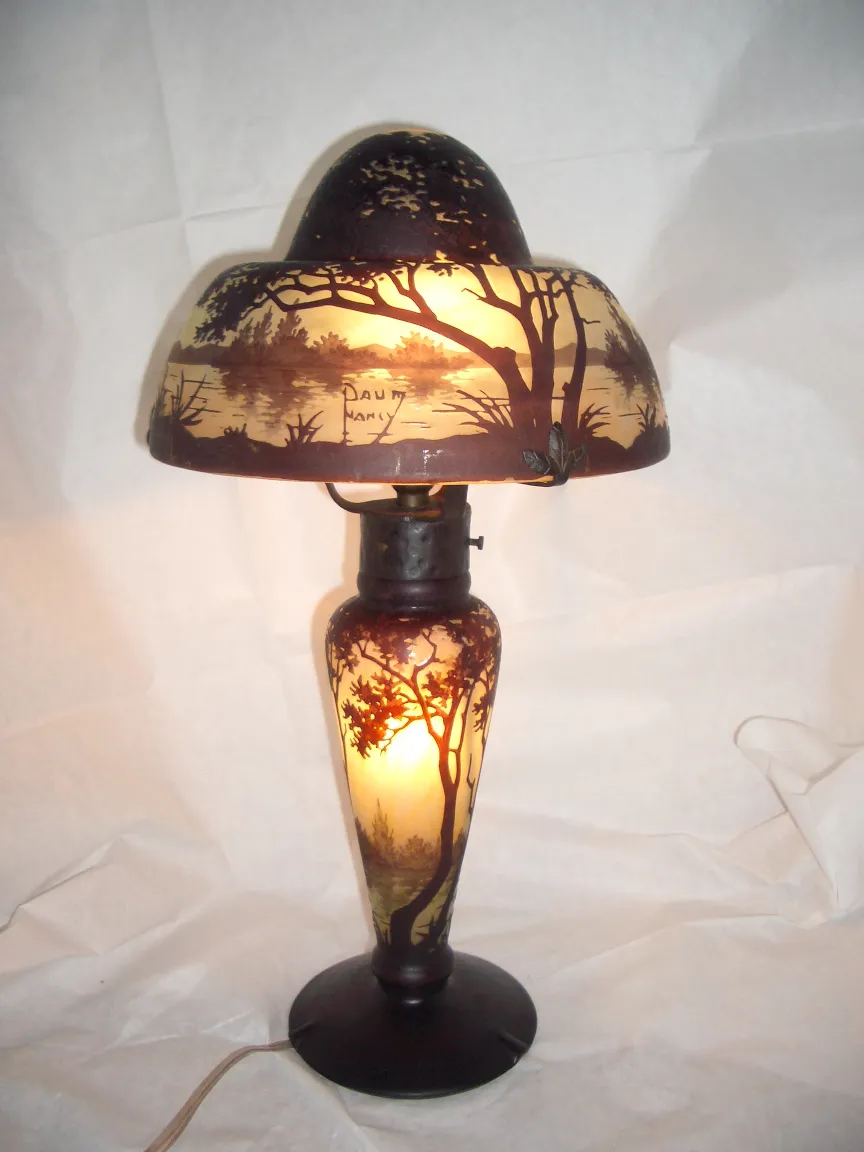 Lampe antique avec verre signé Daum Nancy, motif d'arbre et paysage sur l'abat-jour.