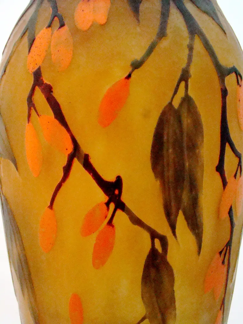 Verre signé Daum Nancy présentant des détails de branches et de feuilles en teintes orange et marron.