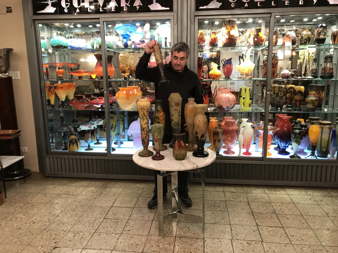 Vasos antiguos de vidrio, algunos con decoraciones, en una exhibición. Hombre sosteniendo una pieza.