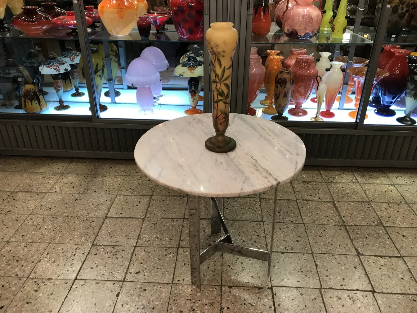 Verre signé antique Daum Nancy sur une table décorative, avec des vases colorés en arrière-plan.