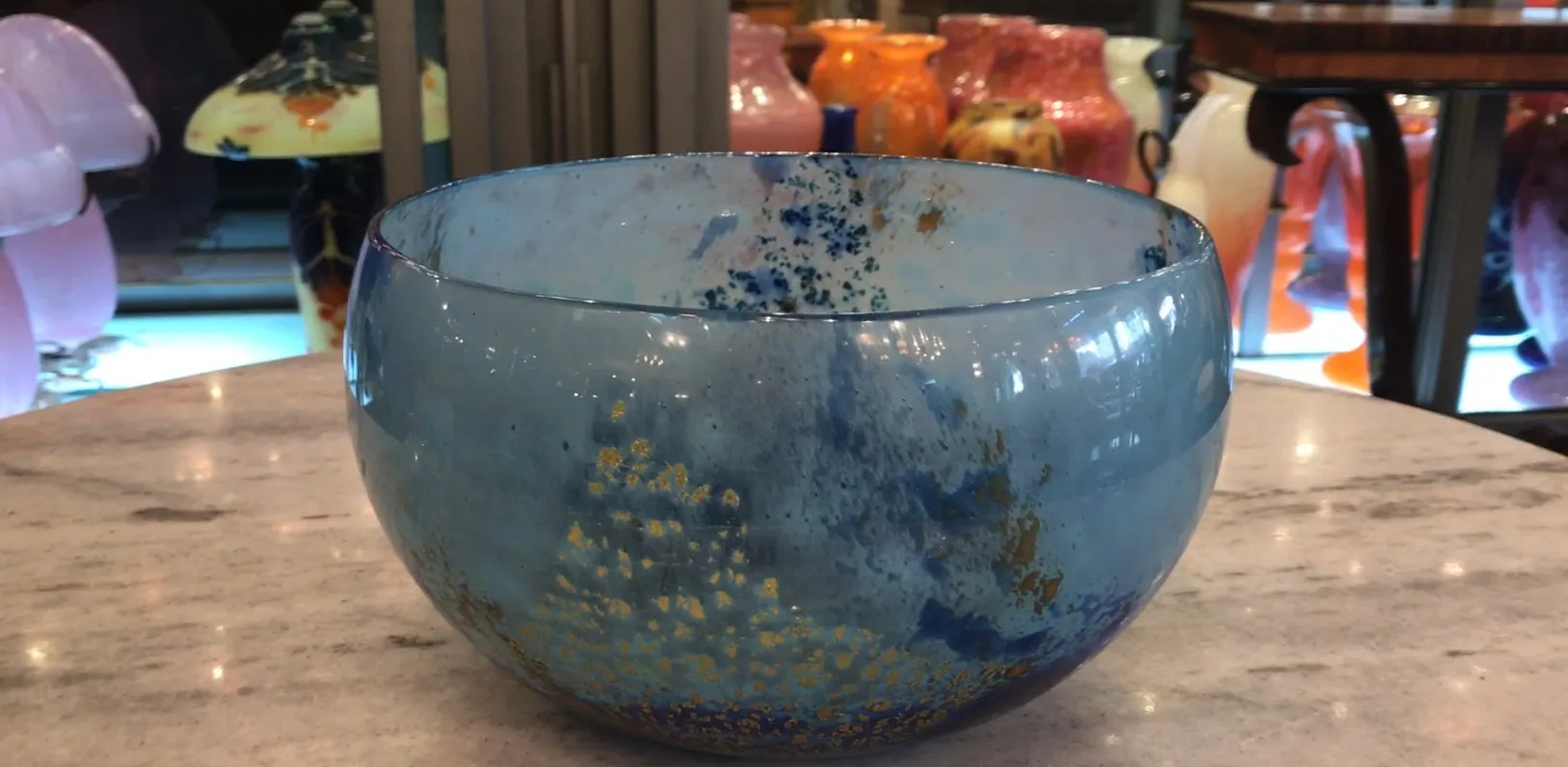 Verre décoratif signé Daum Nancy en nuances de bleu et d'or sur fond blanc.