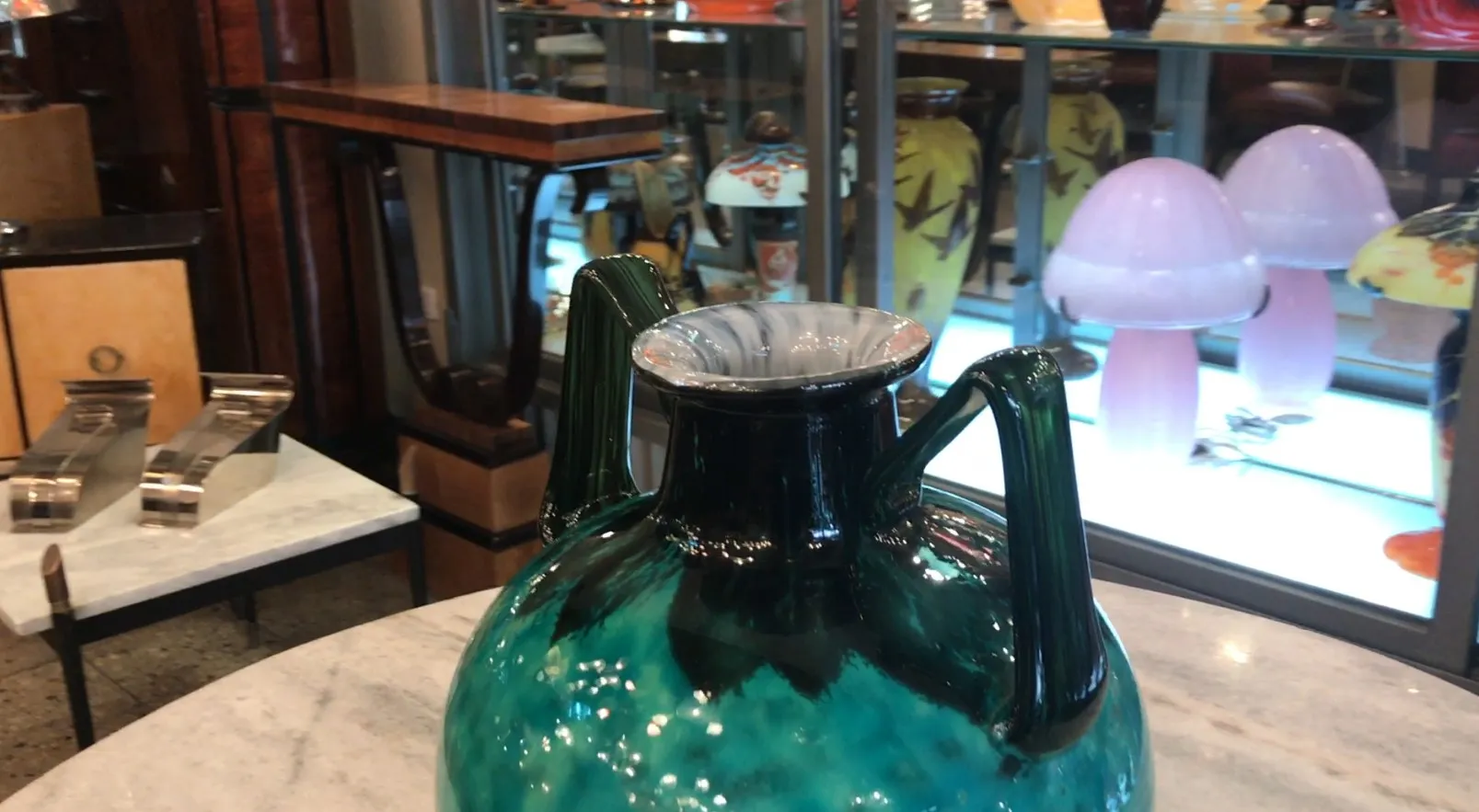 Green pitcher with handles, glossy finish, surrounded by various antique items.