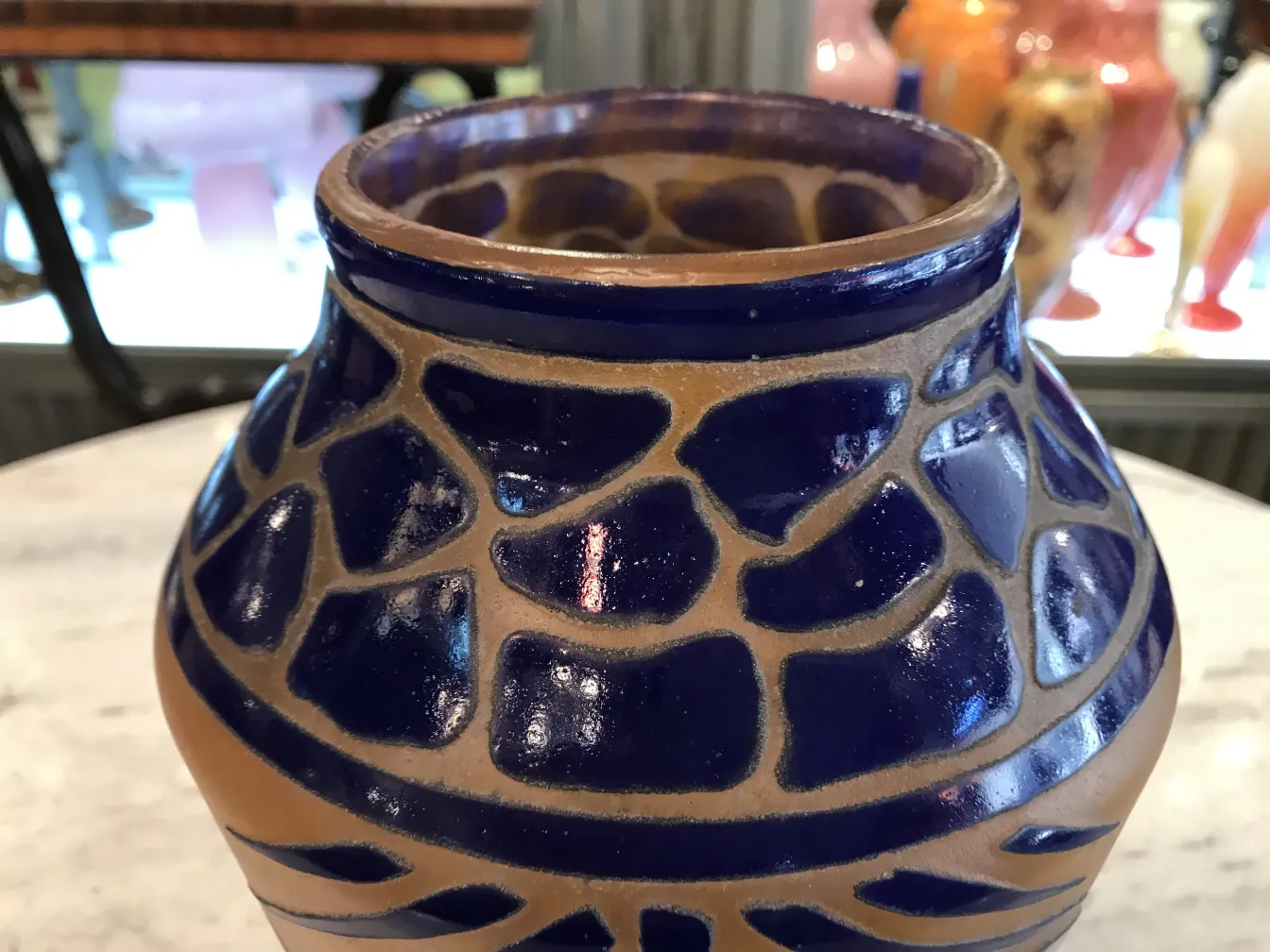 Vaso antico con design blu e beige, pezzi decorativi sullo sfondo.