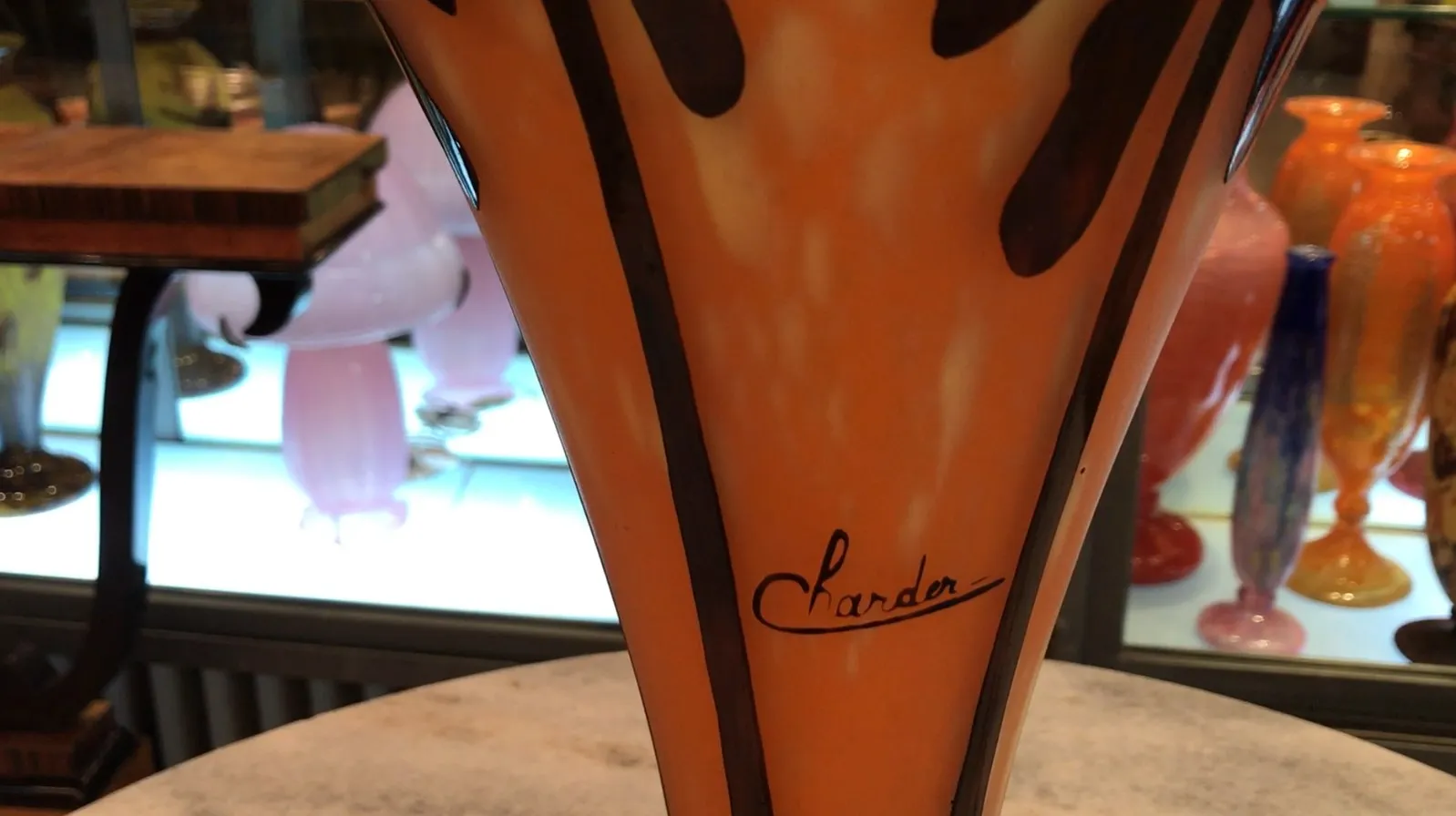 Vidro antigo assinado por Charder com tons laranja e detalhes decorativos, em um ambiente de antiguidades.