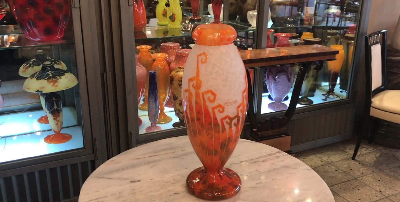 Verre signé Charder avec un design vibrant dans des tons chauds, exposé parmi d'autres objets anciens.