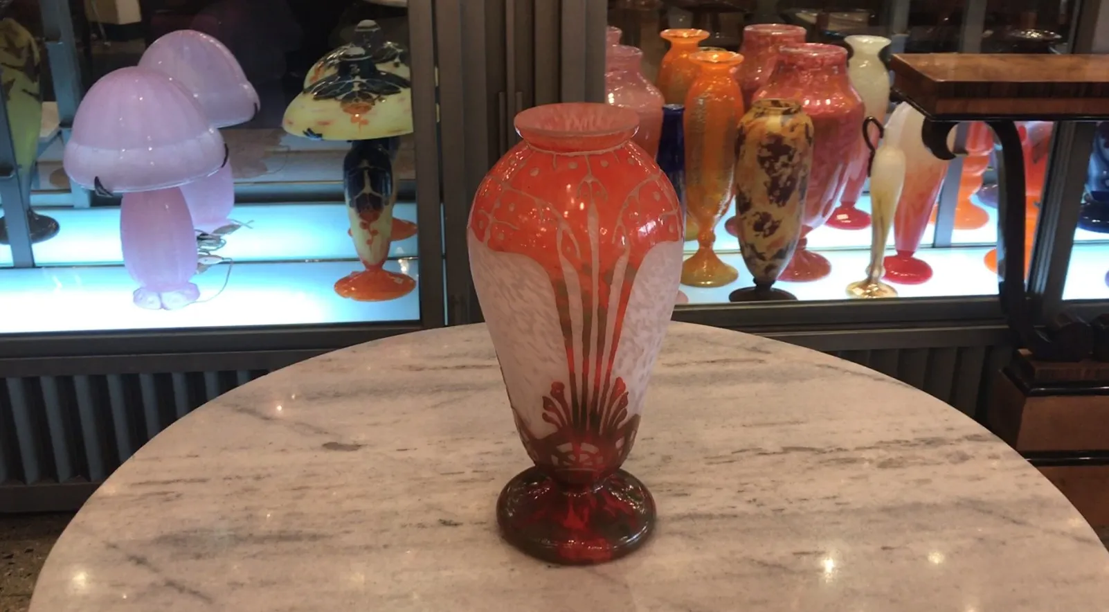 Signiertes Glas Charder in einem antiken Ambiente mit bunten Objekten im Hintergrund