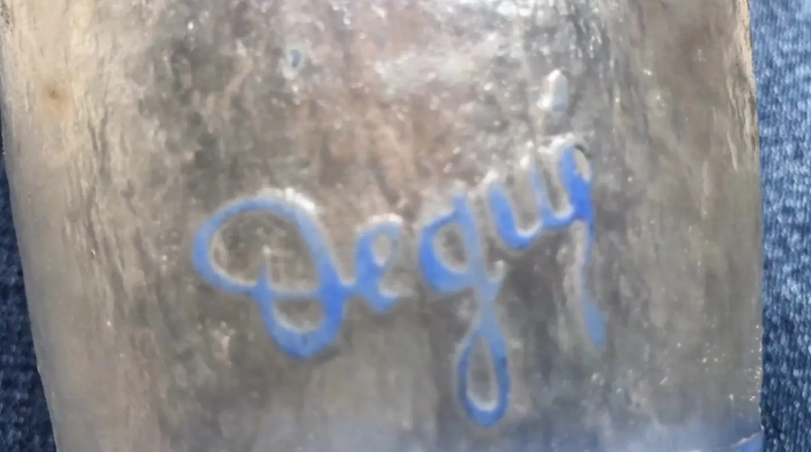 Antikes signiertes Glas Degué mit blauer Inschrift, warme Atmosphäre.