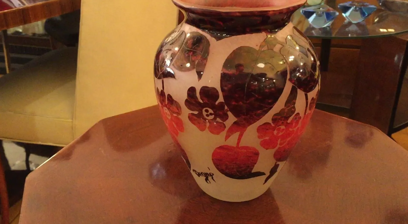 Vaso antico in vetro firmato Degué con fiori decorativi, sfondo di tavolo in legno.