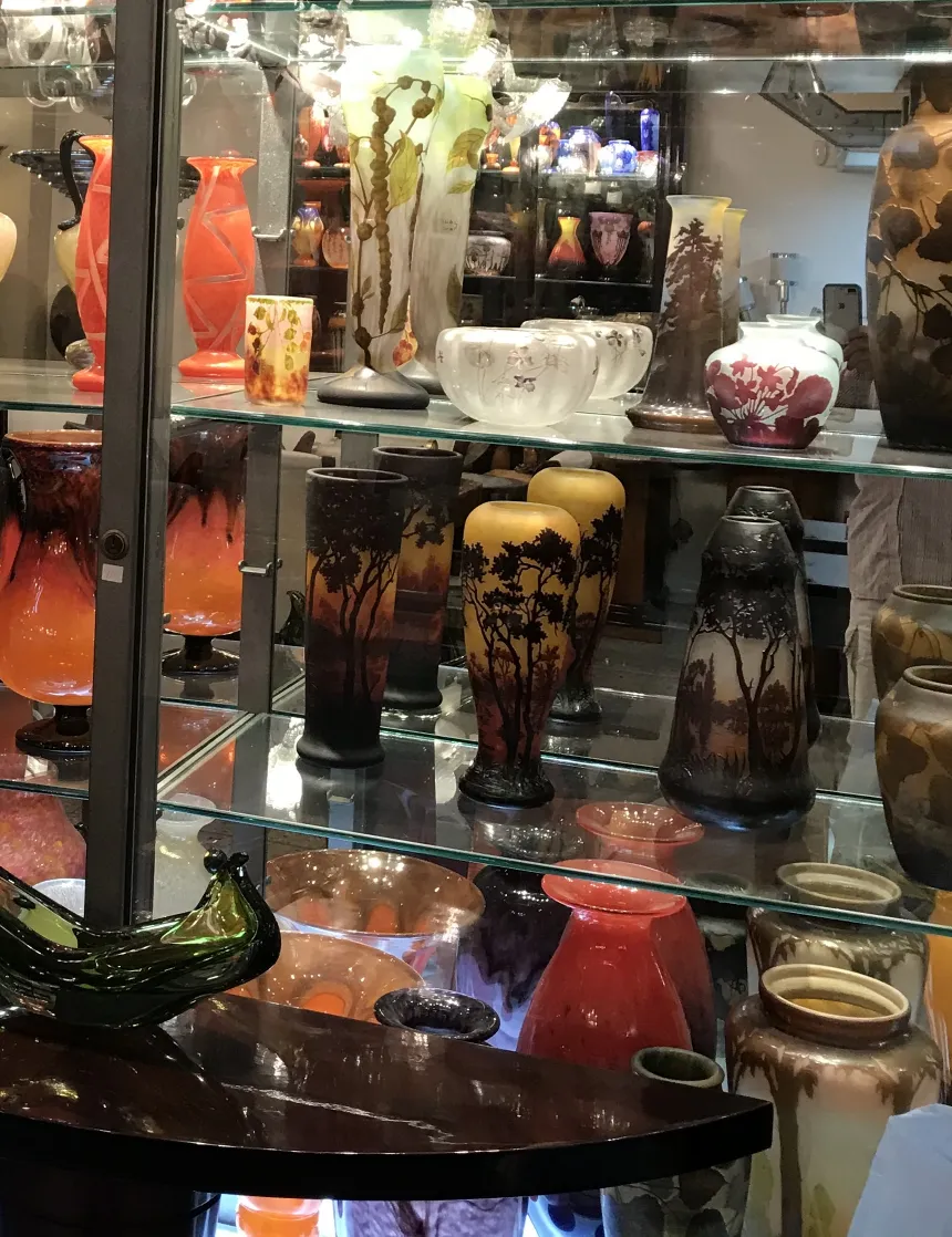 古い風景色のサイン入りグラス（Degué）が展示ケースにあり、他のアンティークに囲まれています。