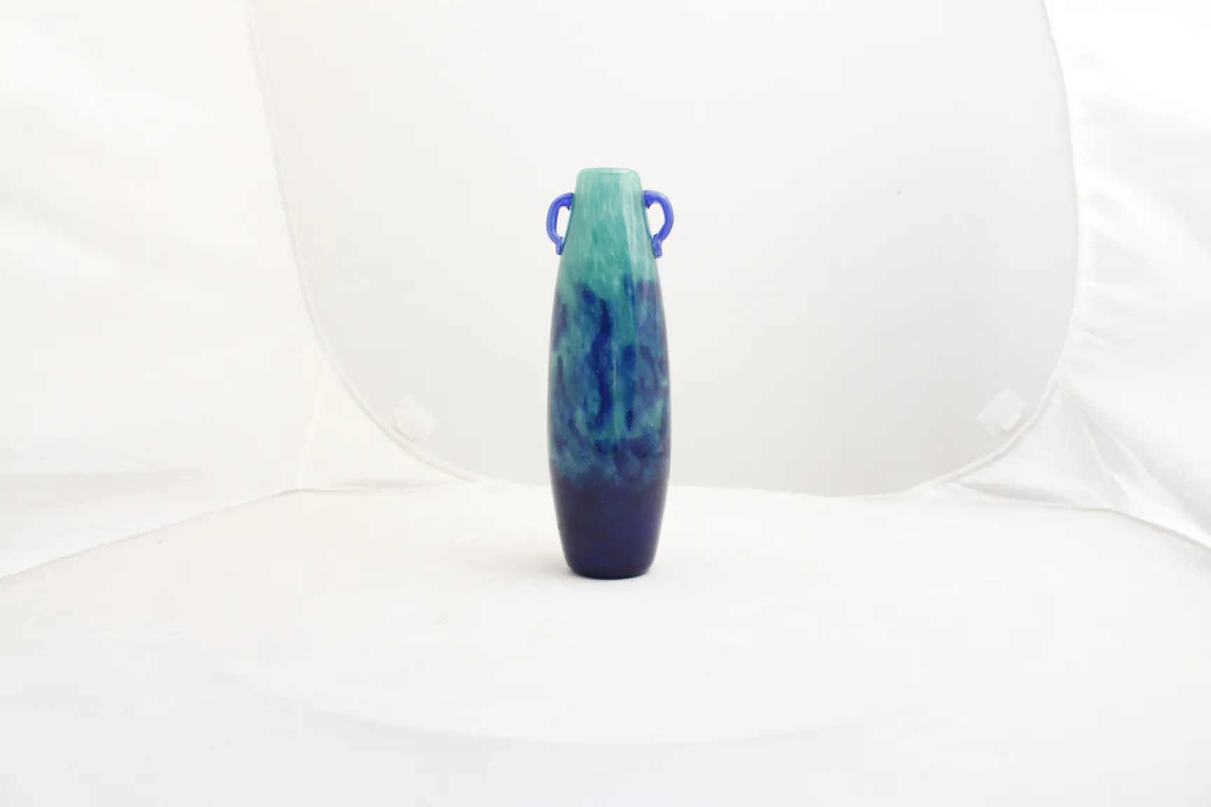Vase en verre signé Degué de teintes vertes et bleues, avec un design décoratif, sur fond blanc.