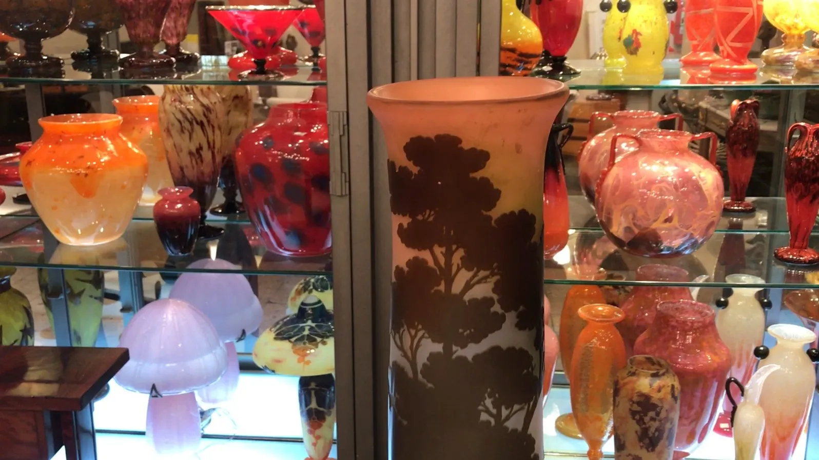 Vaso antiguo firmado con decoración de árboles, exhibido con otros objetos coloridos