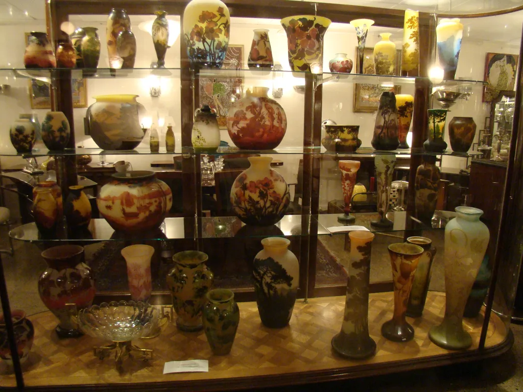 Collection of antiques on display, including signed glass Gallé and other decorative vases in various colors.