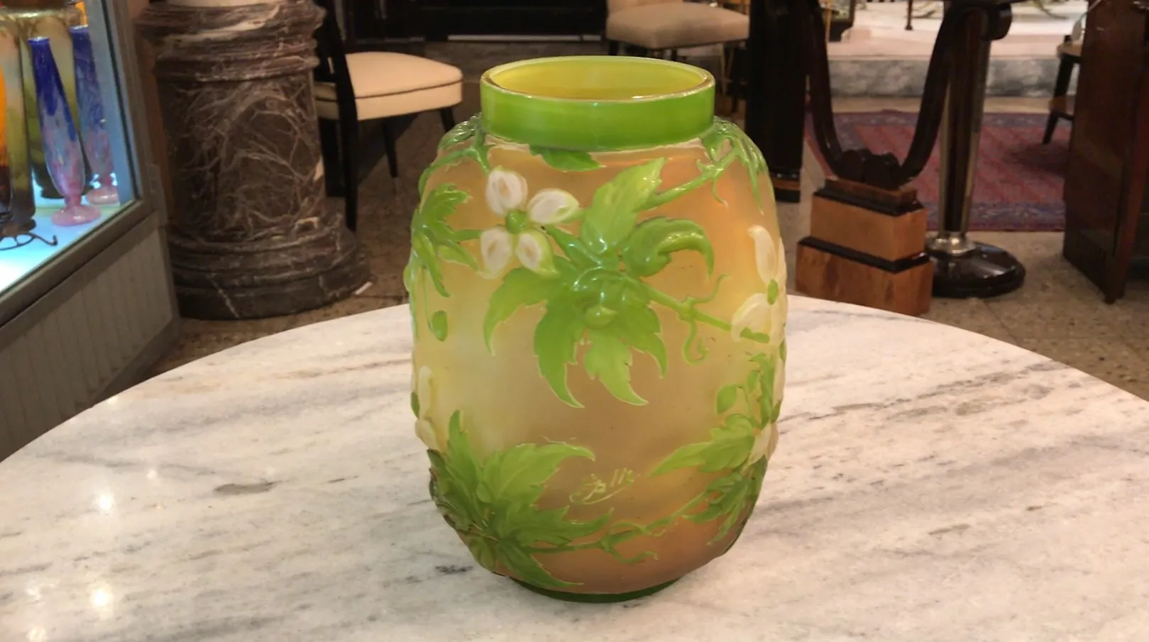 Signiertes Glas Gallé mit grünem Blumenmuster auf hellem Hintergrund, in antikem Ambiente präsentiert.