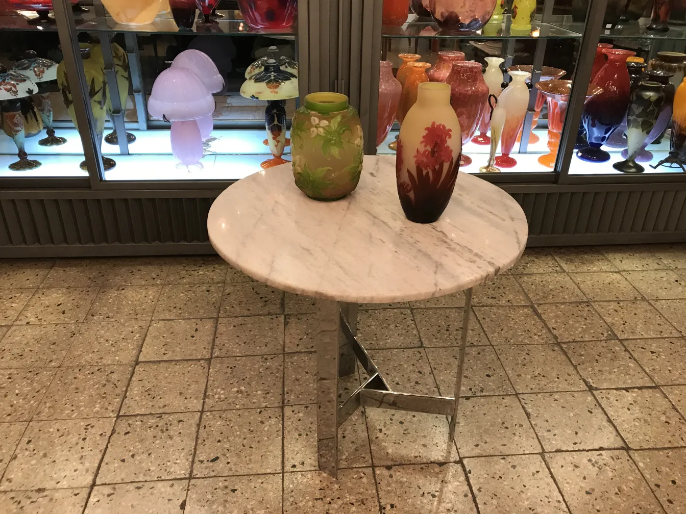 Verre signé Gallé sur une table en marbre, avec une décoration colorée autour.