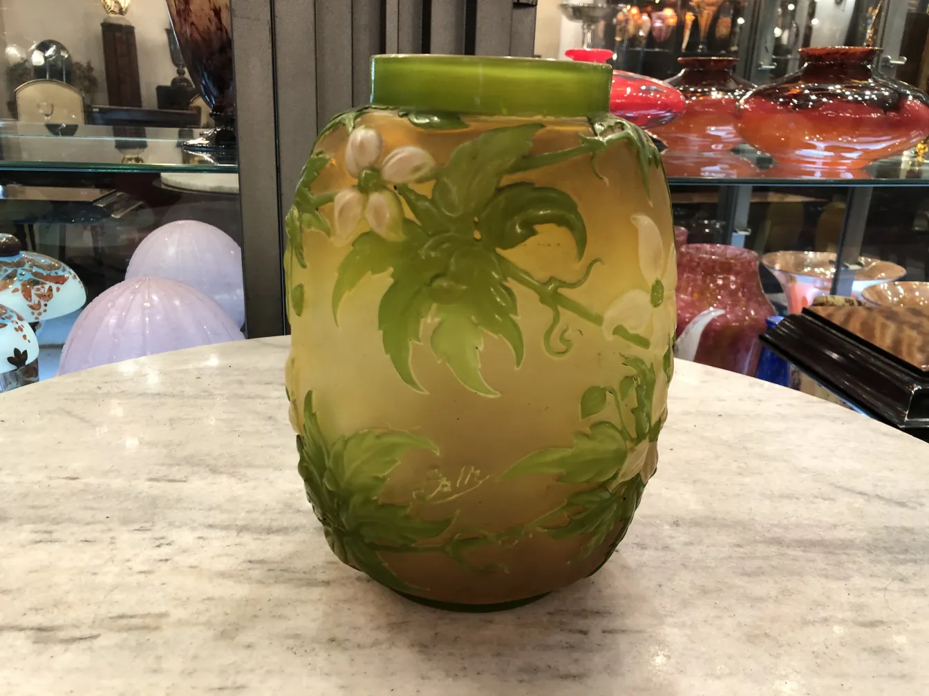 jar décoratif ancien signé par Gallé avec décoration florale sur fond clair, parmi d'autres objets en verre