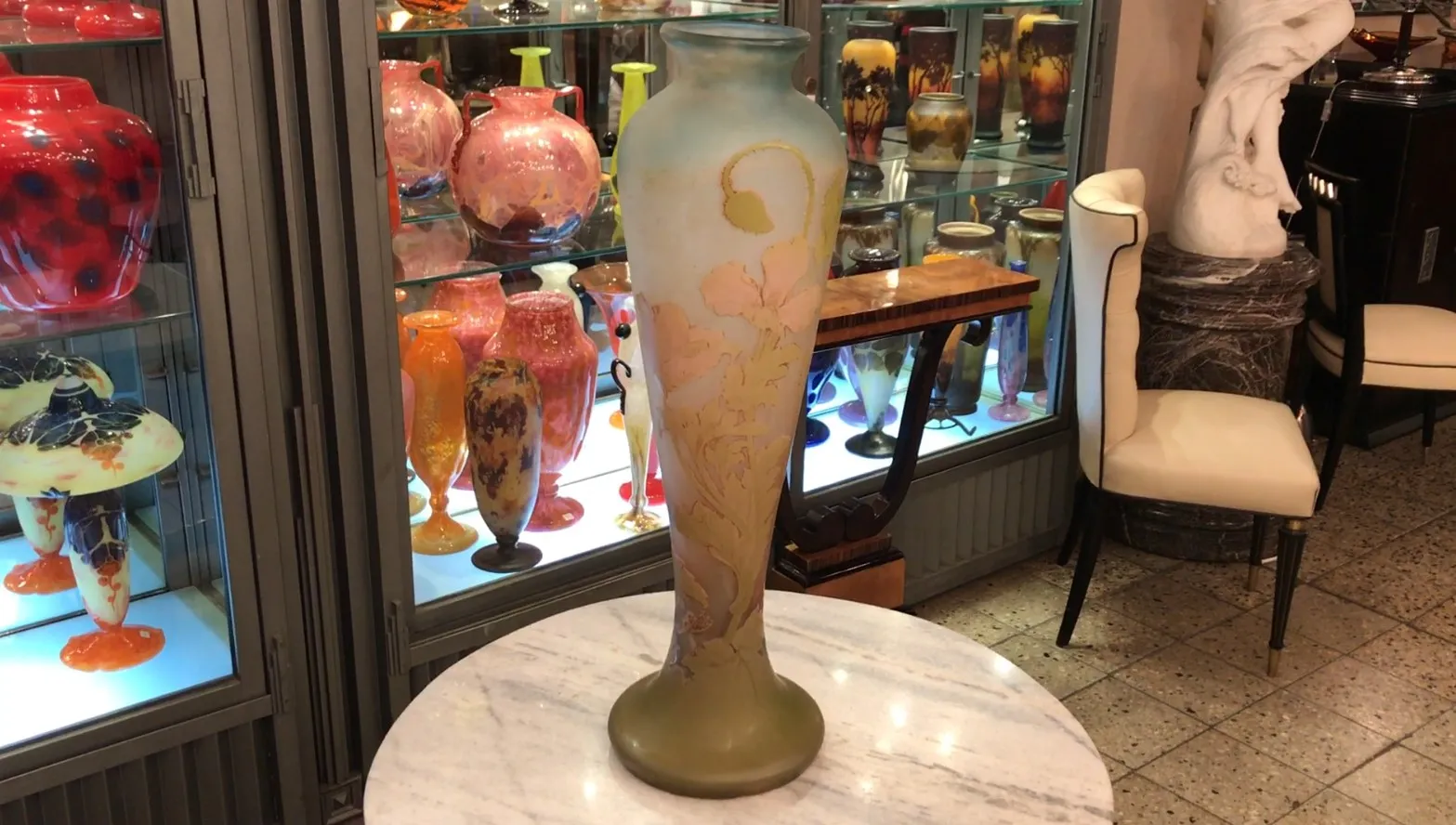 Antique signed glass Gallé displayed in a showcase, with colorful glass objects in the background.
