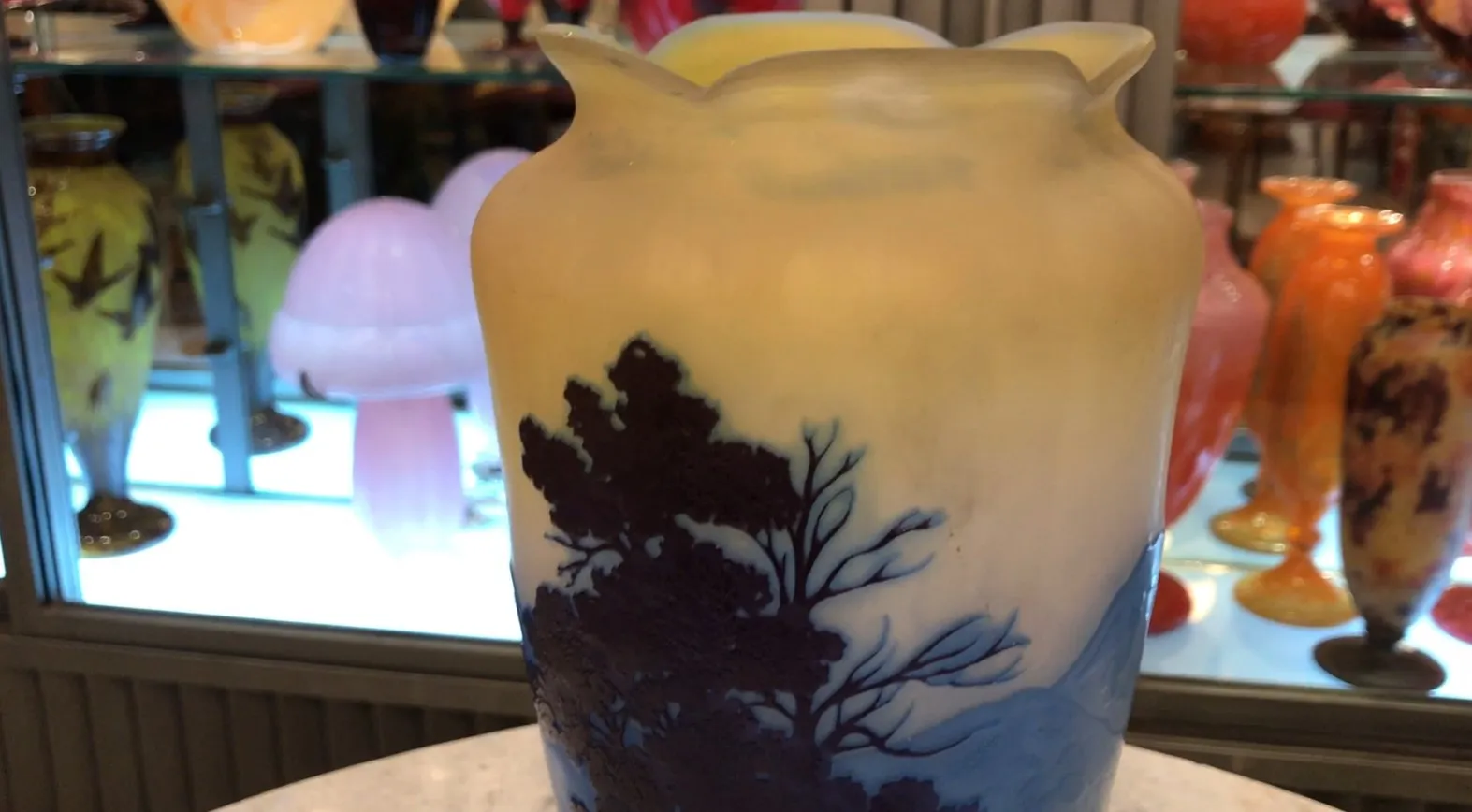 Antike Vase mit naturalistischem Design in Gelb- und Blautönen, signiert von Gallé, umgeben von anderen dekorativen Gegenständen.