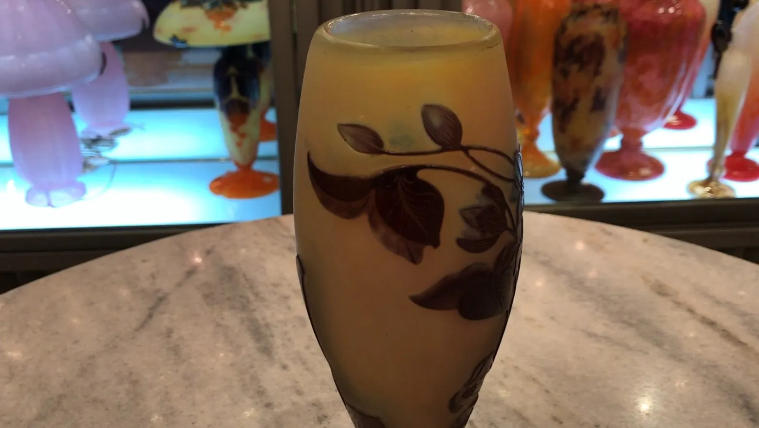 Vaso con design di foglie in giallo e marrone, sfondo con altri oggetti antichi.