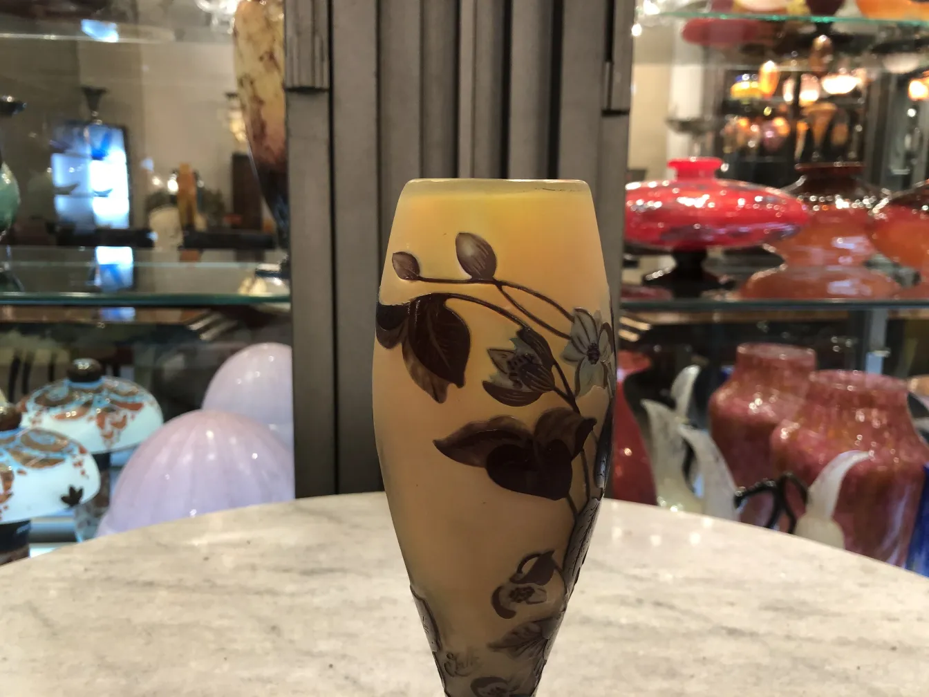 Vaso de vidrio firmado de Gallé con decoración de flores, en fondo de exhibición de antigüedades.