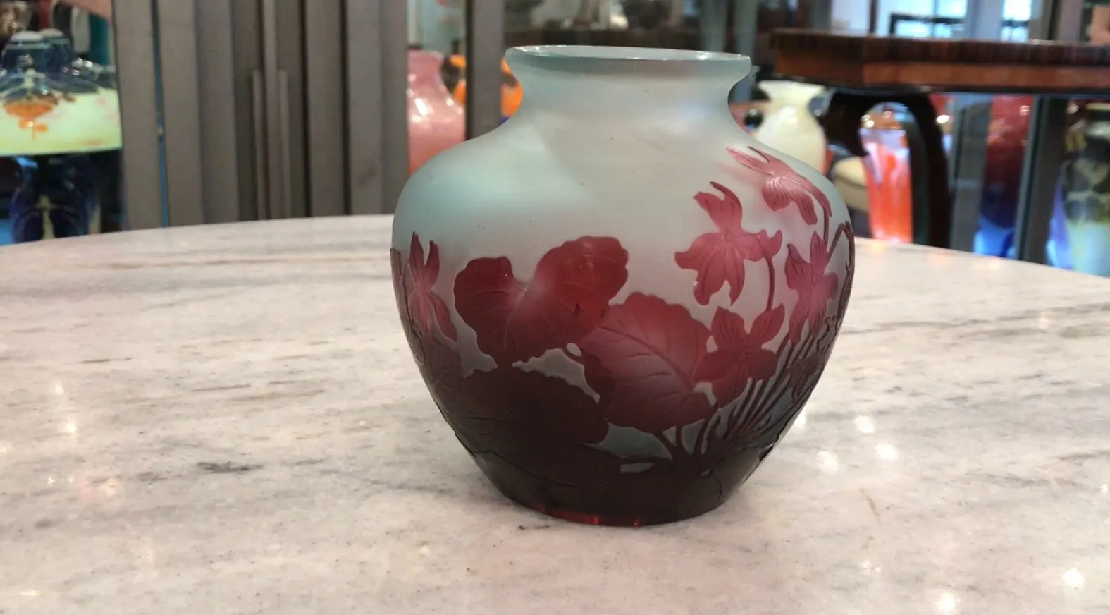 Vaso in vetro firmato Gallé con decorazione floreale in tonalità rosse e blu, ambiente elegante.