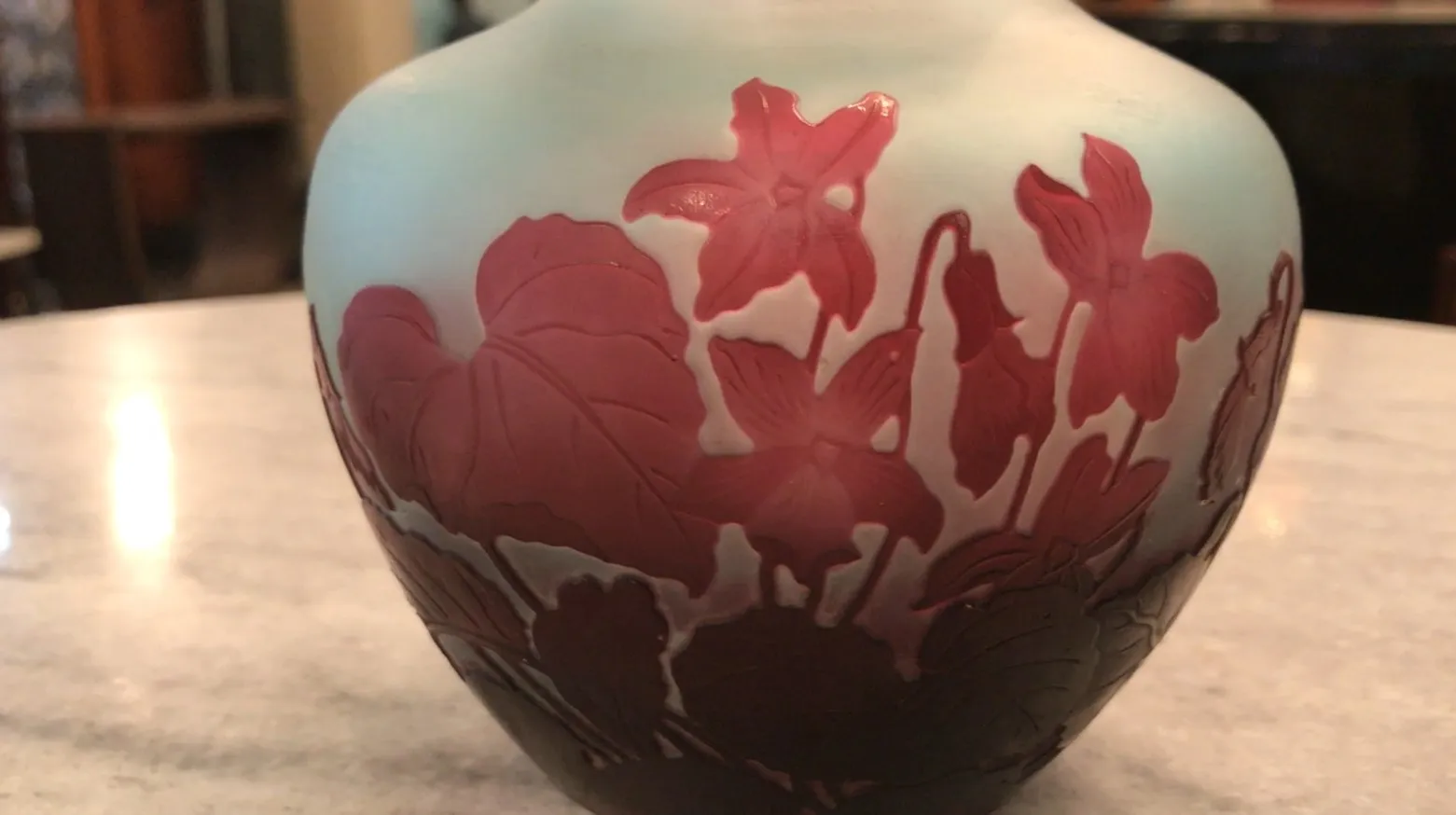Vase en verre signé Gallé avec motif floral en teintes rouges et bleues, exposé sur une surface claire.