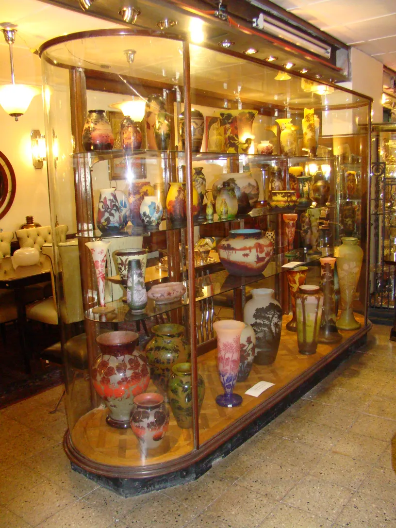 Vidro assinado Gallé exposto em vitrine com outros itens antigos coloridos.