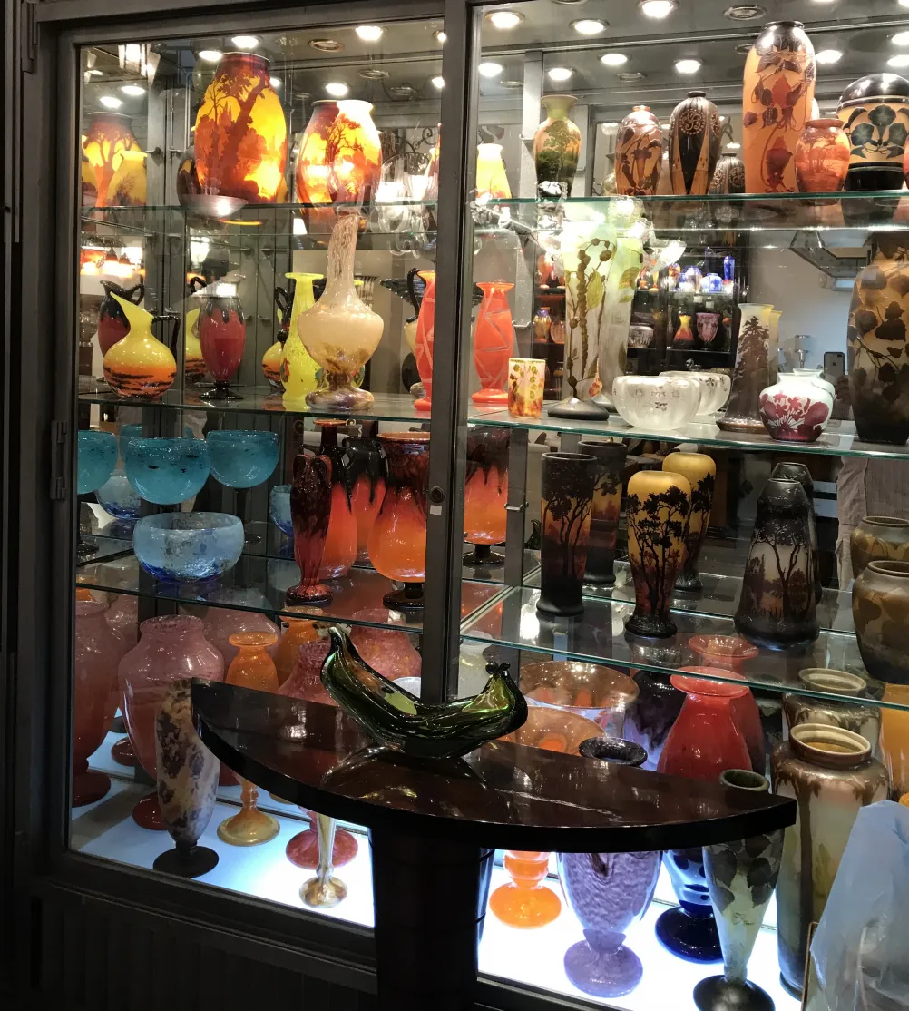 Exposición de antigüedades incluyendo vidrio firmado D'Argental, variedad de colores. Ideal para colección.