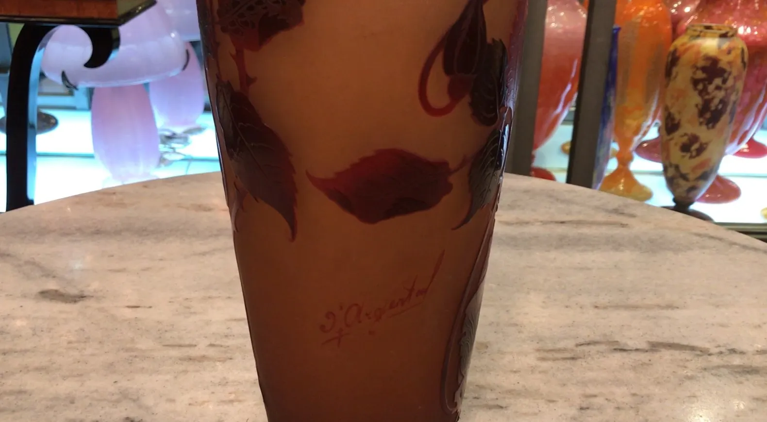 Vidrio firmado D'Argental con diseño de hojas rojas en fondo claro, en ambiente de antigüedades.