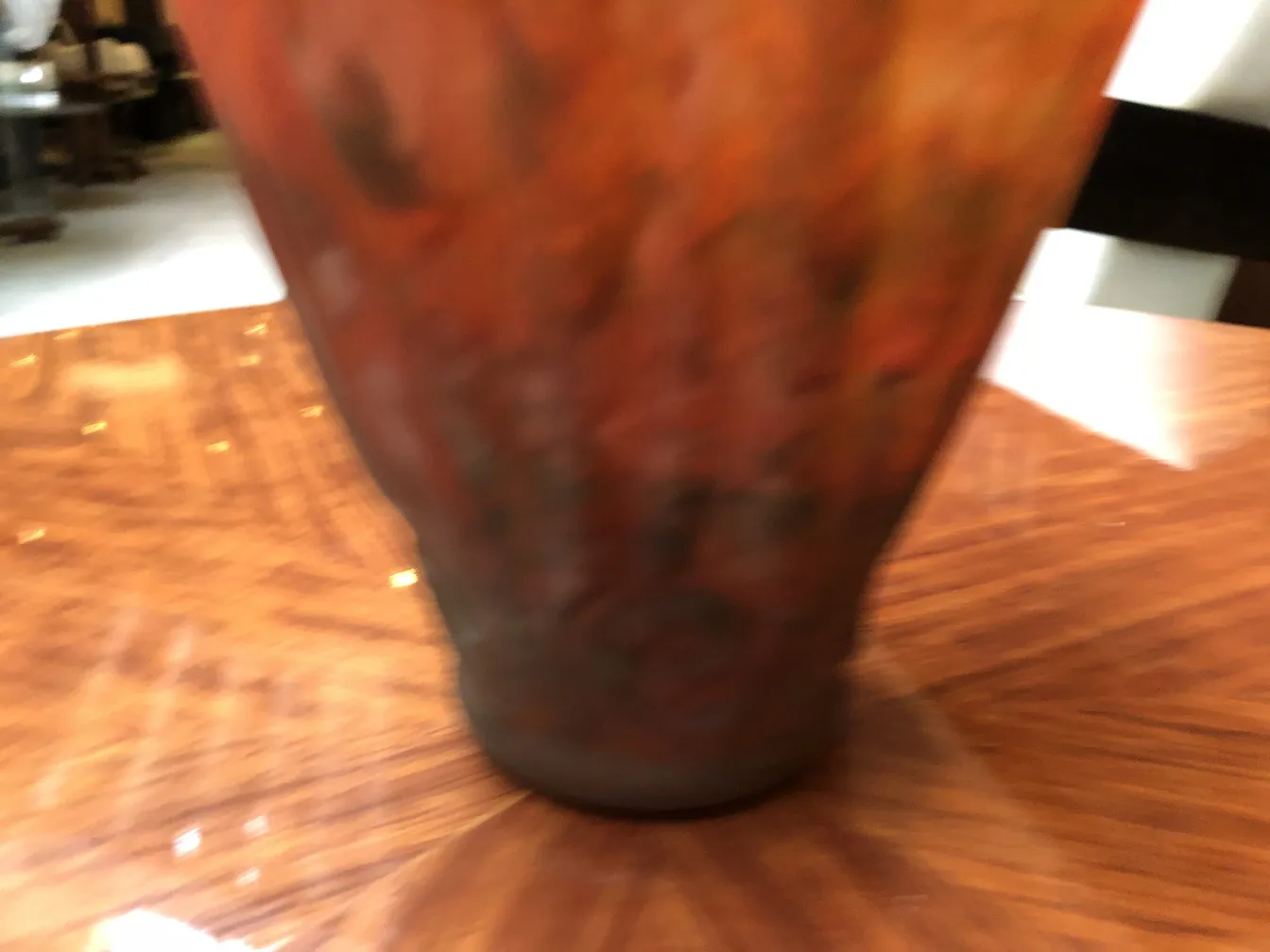 Antique glass with unique design, reddish and orange hues, set on a dark wooden table.