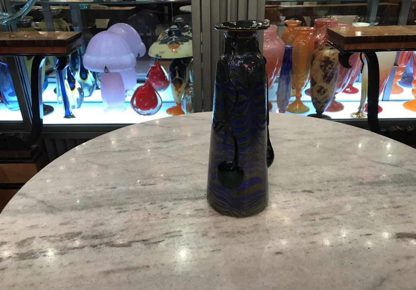 Bouteille ancienne en verre signé Loetz avec motif bleu et noir sur une table en marbre.