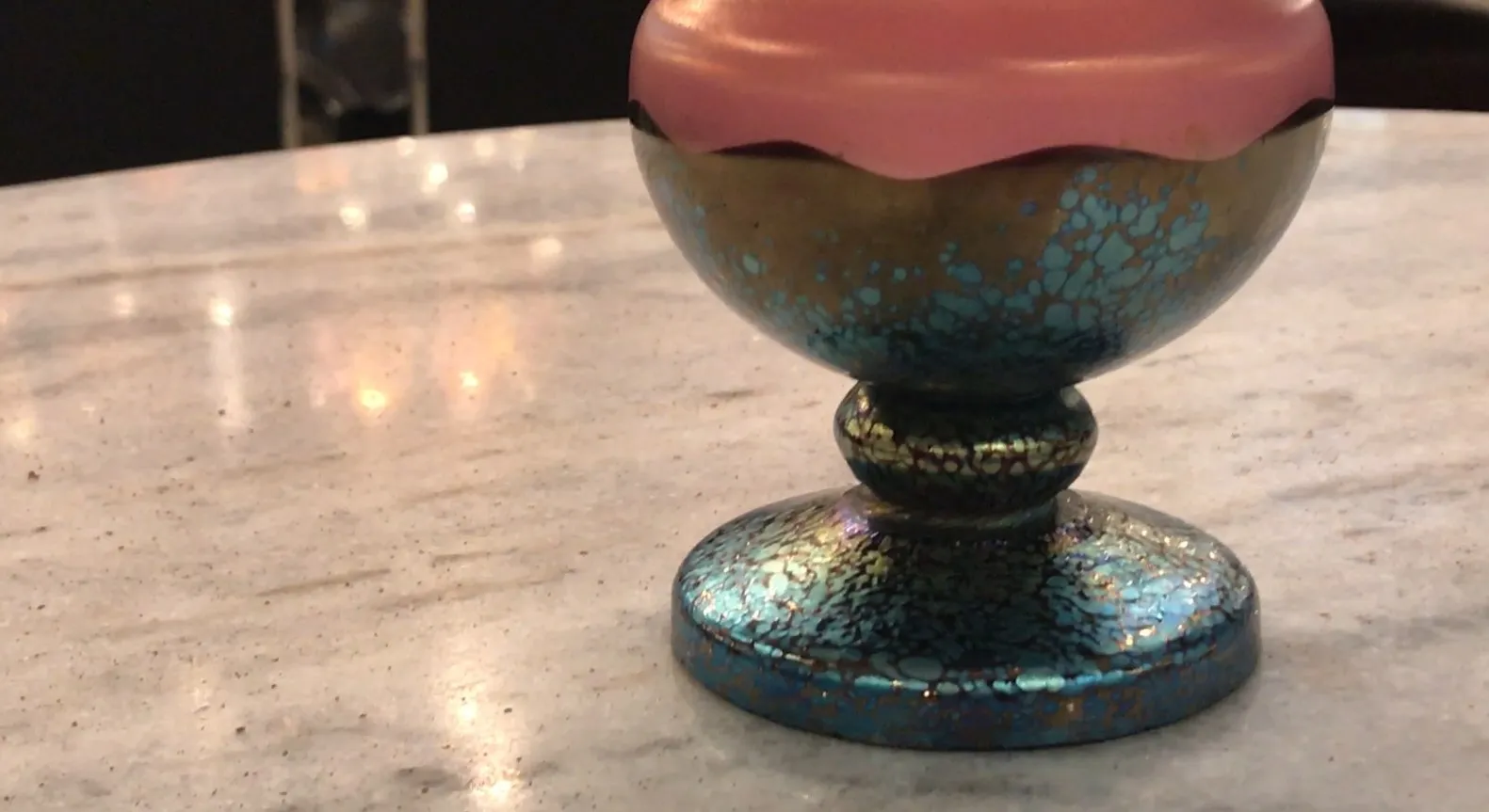 Coupe ancienne en verre signé Loetz avec des détails colorés, sur une table claire avec un fond flou