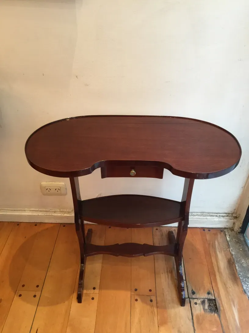 Petite table antique avec dessus ovale et pieds décoratifs, fond neutre.