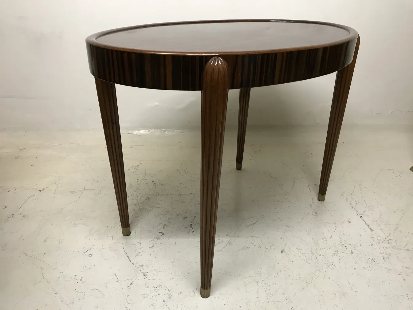 Mesinha antiga com pernas elegantes e formato oval em um ambiente claro.