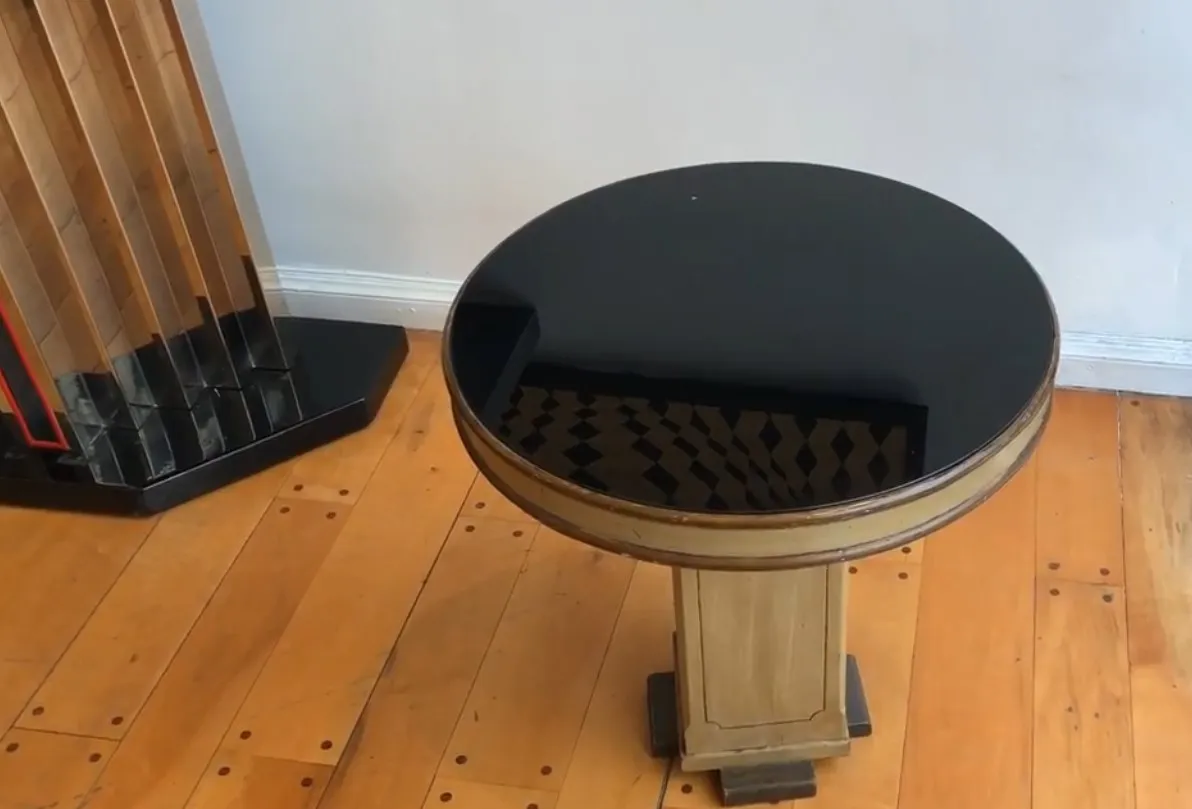 Antique round small table with a dark finish, situated in a cozy setting with light wooden floor.