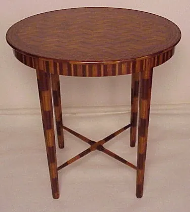 Mesita redonda antigua con un diseño de zigzag en la parte superior y patas decorativas.