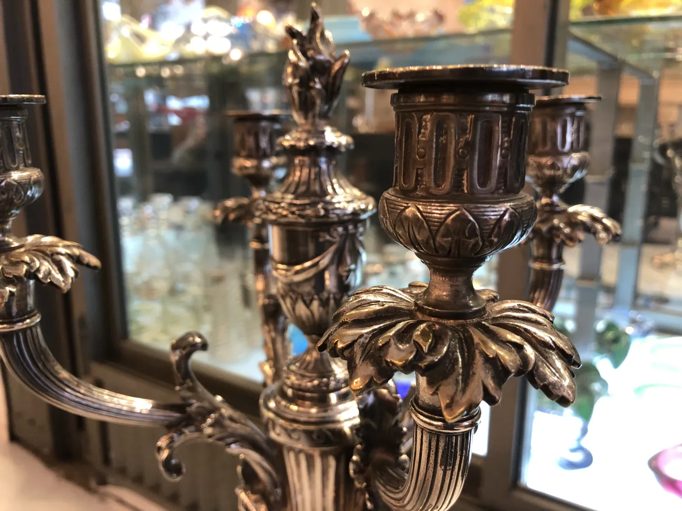 two candlesticks with leaf and flower details, background with glassware