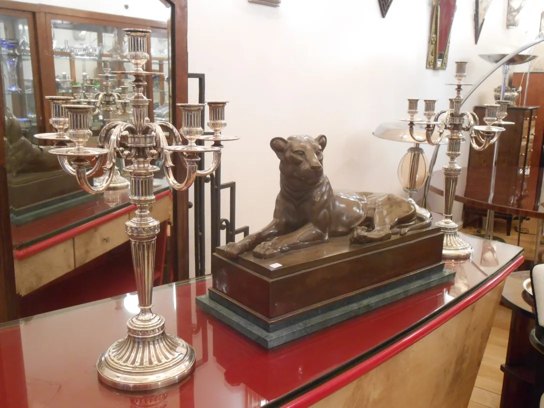 Deux candélabres anciens sur une table élégante, avec une statue de lion en arrière-plan.