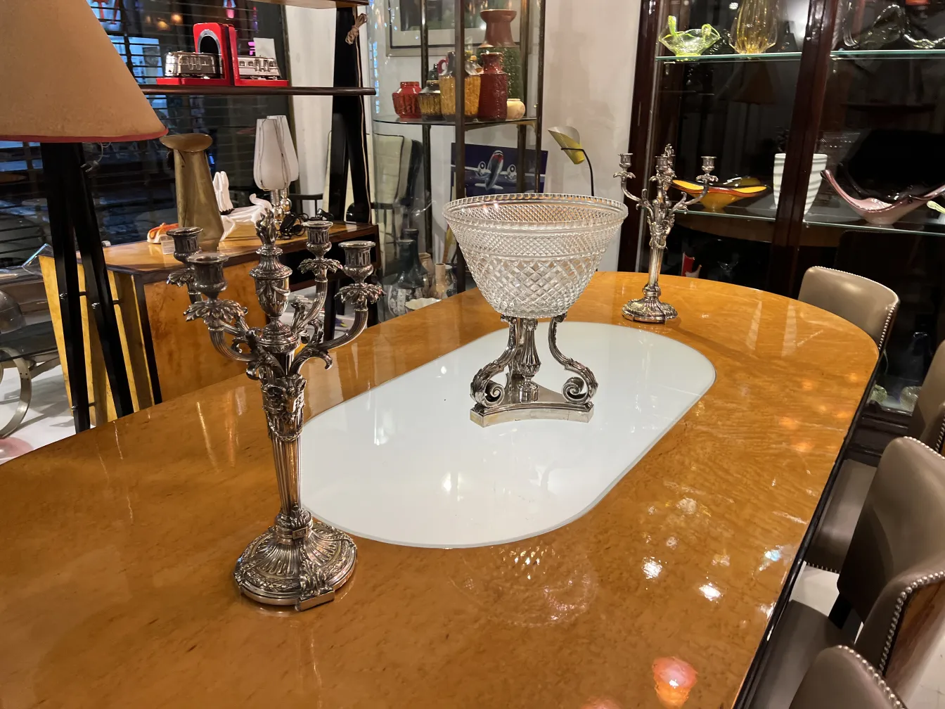 florero antiguo con forma elegante y detalles ornamentales, rodeado de candelabros plateados en una mesa