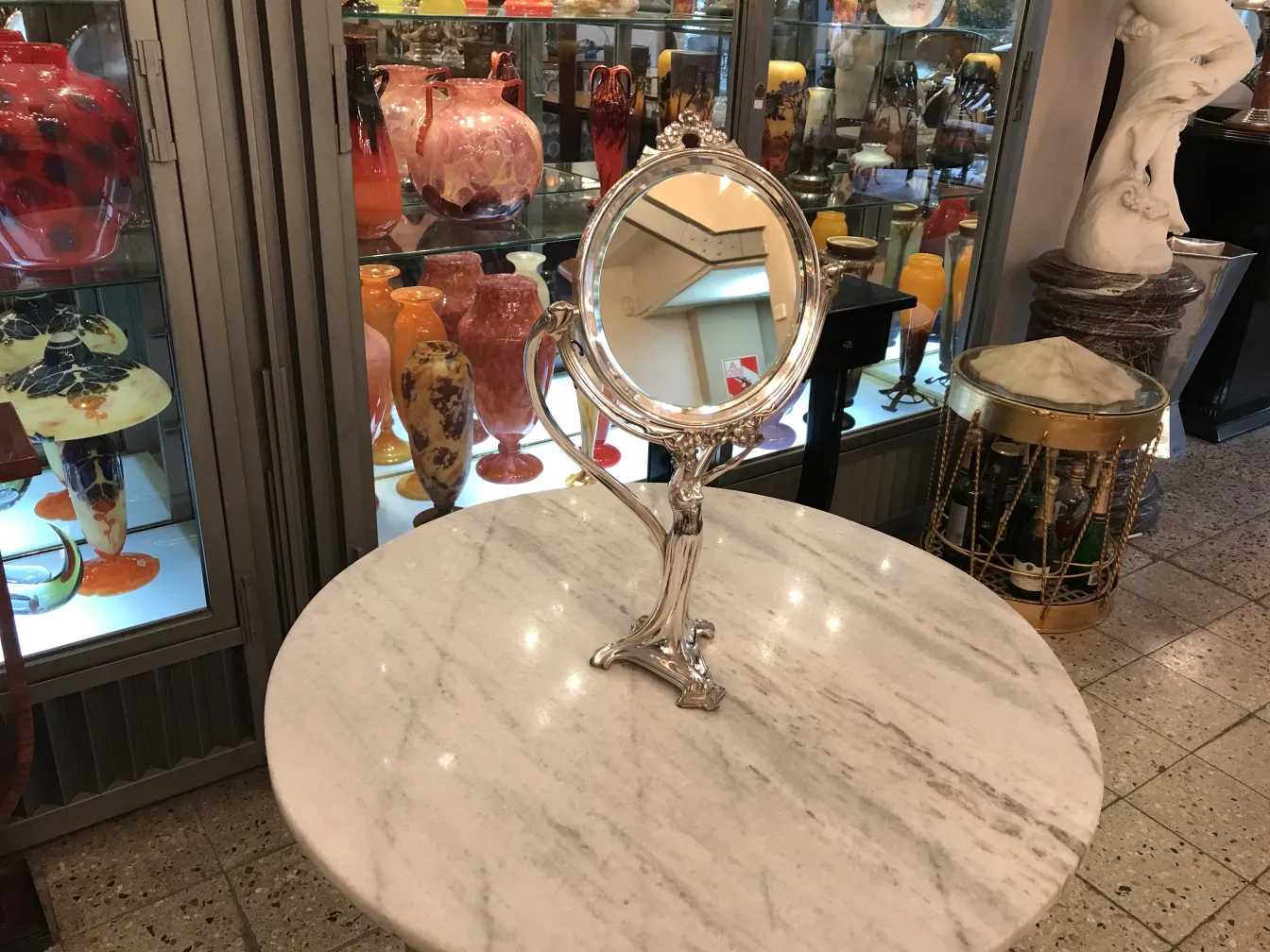 Espejo antiguo con ornamentos en base de art nouveau, fondo con jarrones coloridos.