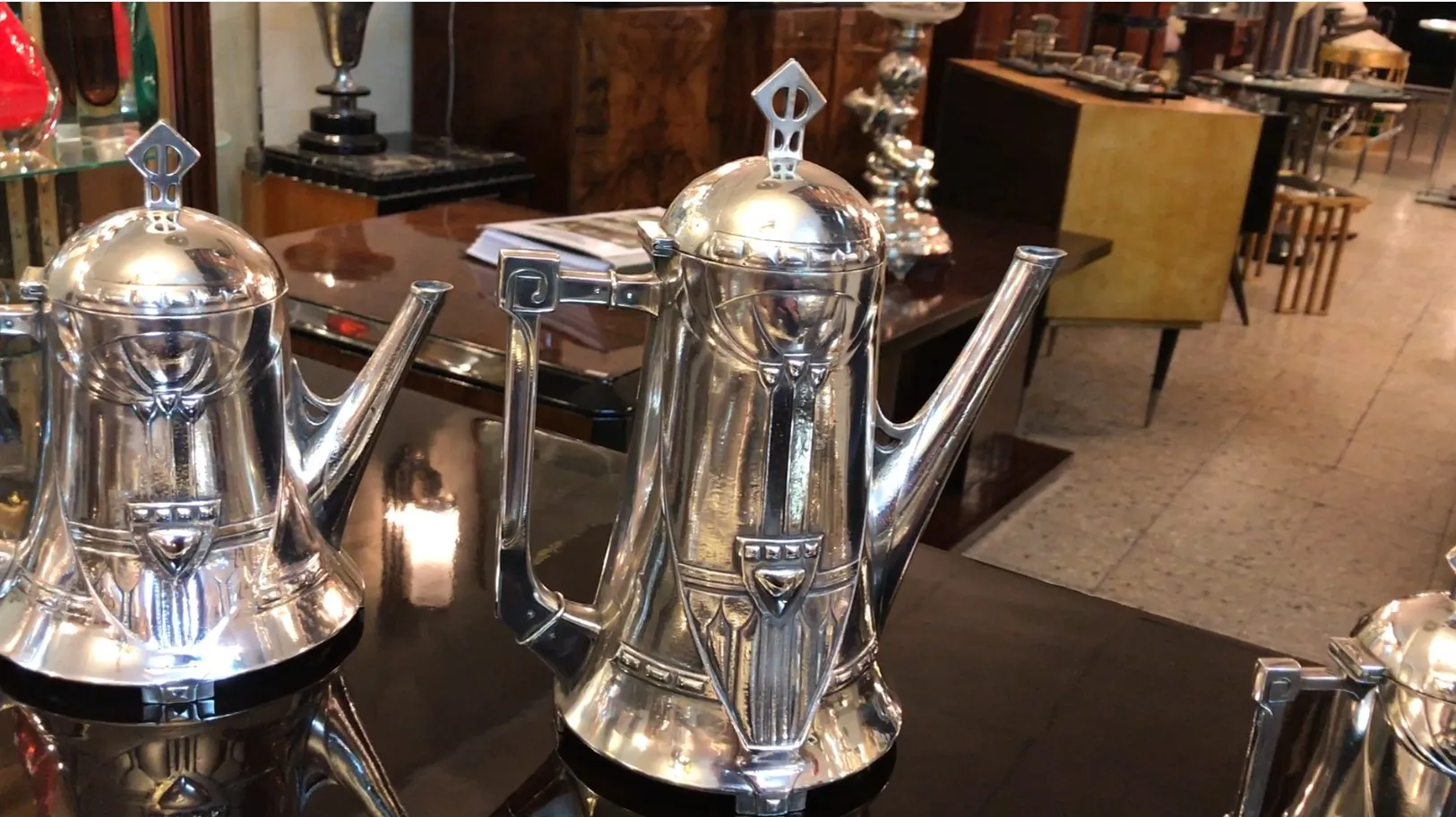 Set da tè antico WMF con finitura lucida, esposto su un tavolo di legno, con altri oggetti decorativi sullo sfondo.