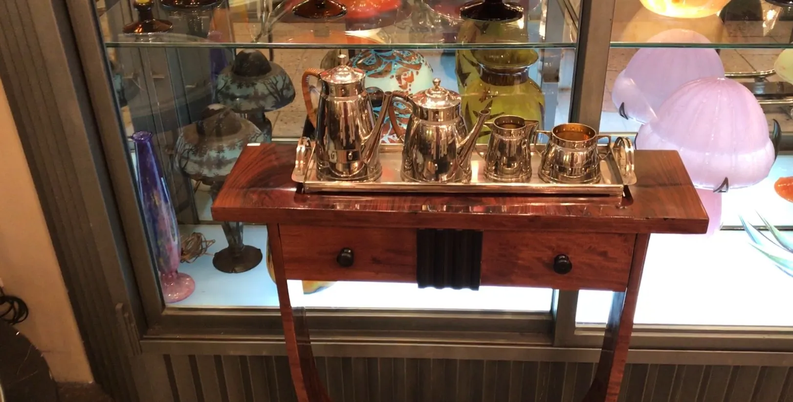 Juego de té antiguo WMF sobre una bandeja plateada, decorado con vajillas de colores al fondo.